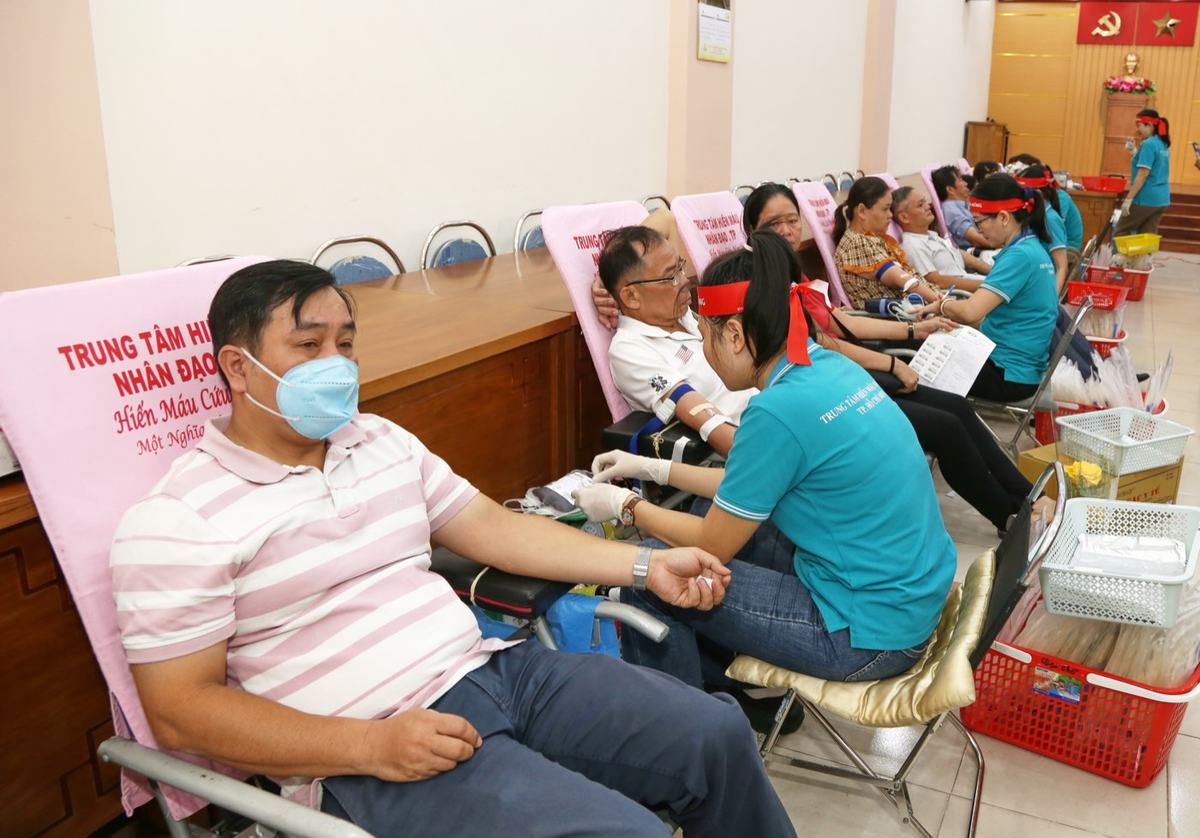 Người dân ngồi trên ghế hiến máu, nhân viên y tế áo xanh đang hỗ trợ tại điểm hiến máu tình nguyện